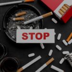 Card with the word stop resting on an ashtray filled with cigarette butts surrounded by pills syringes and a red cigarette packan anti substance abuse message