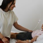 Caregiver sits at the bedside smiling holding the hand of a young girl in a hospital bed with an iv line