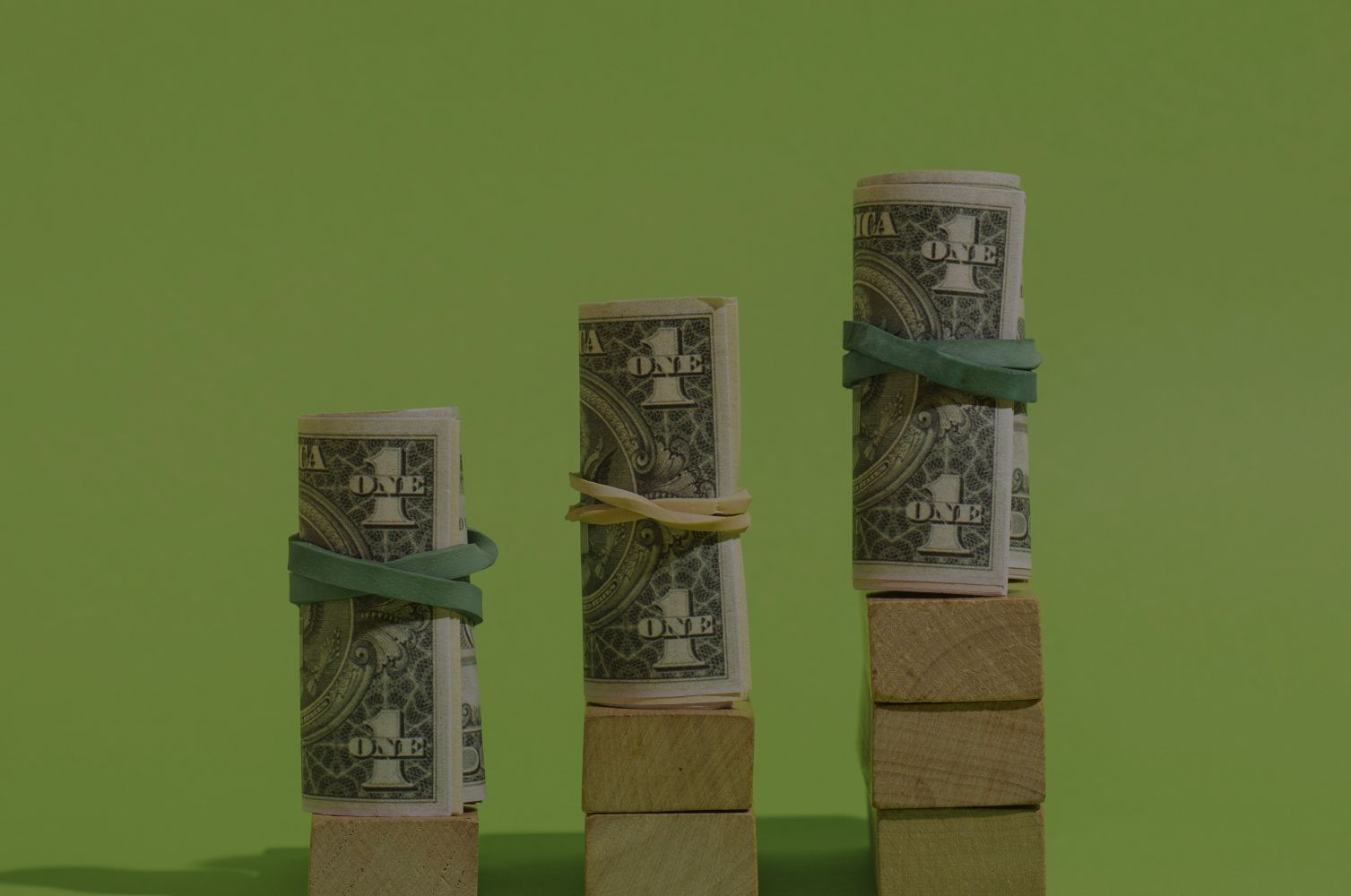 28edolar catrawarta Stacks of rolled dollar bills bound with rubber bands on wooden blocks increasing in height from left to right against a green background growthsavings