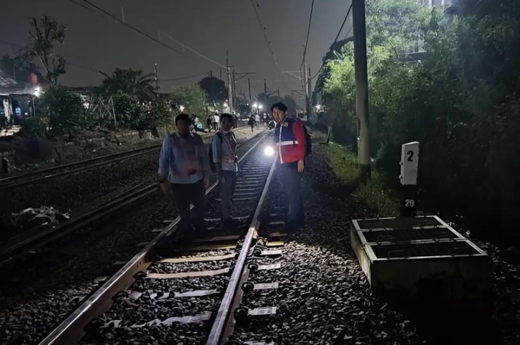 Nighttime rail scene with several people standing on tracks one person in a red safety vest near a signal box