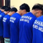 Group of men in blue t shirts with tahanan polres bantul on the back standing in a line with heads bowed