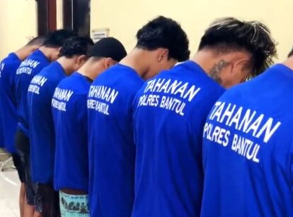 Group of men in blue t shirts with tahanan polres bantul on the back standing in a line with heads bowed