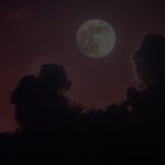 Full moon rising behind dark clouds at dusk with a crimson skymoody night scene