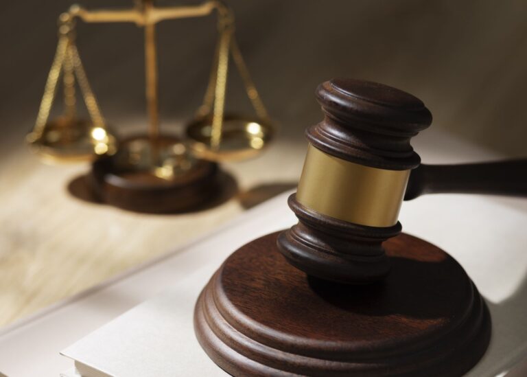 Judge's gavel in the foreground with the scales of justice blurred in the background, symbolizing law and justice.