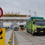 Green truck in the right lane at padang toll gate approaching toll booths beneath a large gerbang tol padang sign