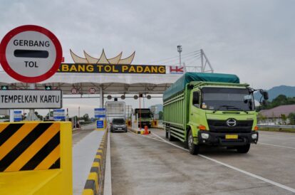 Green truck in the right lane at Padang Toll Gate, approaching toll booths beneath a large 'Gerbang Tol Padang' sign.