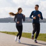 Two runners a woman and a man jogging along a brick path beside a lake on a sunny day with hills in the distance