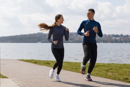 Two runners a woman and a man jogging along a brick path beside a lake on a sunny day with hills in the distance
