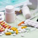 Assorted pills capsules vials and a syringe scattered on a light surface in a medical setting