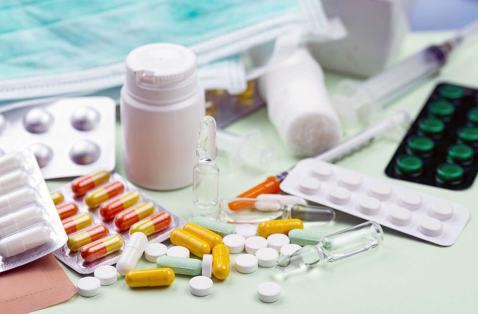 Assorted pills capsules vials and a syringe scattered on a light surface in a medical setting