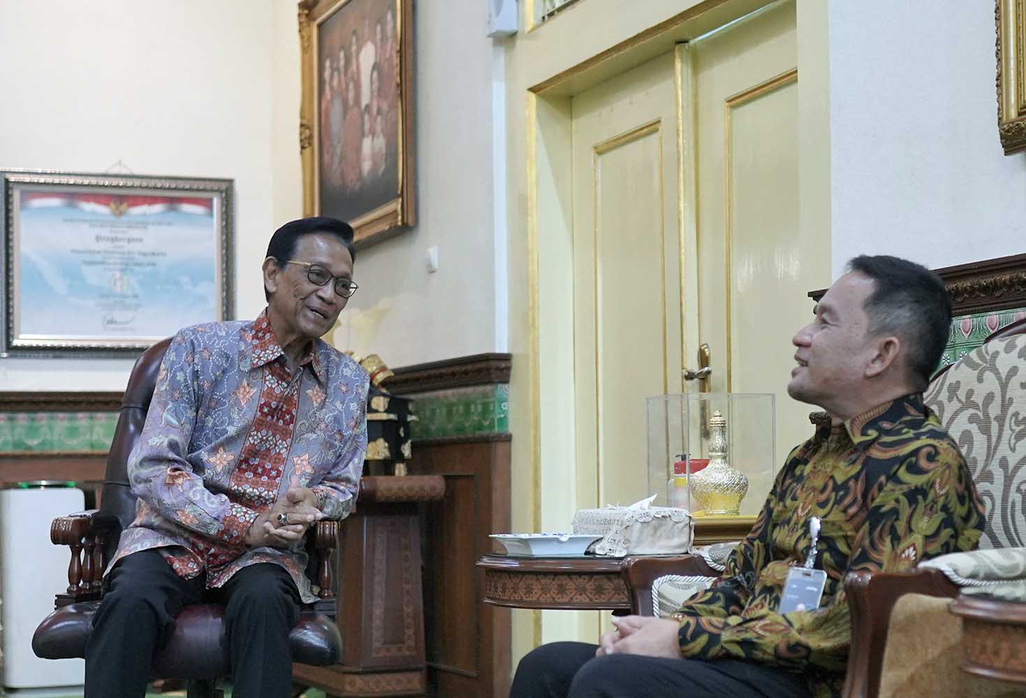 7esultan catrawarta Two men in batik shirts sit and chat in a richly decorated room with gold trim and framed portraits