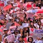 Large crowd of protesters holding colorful signs and banners at a demonstration