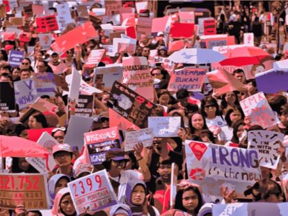 Large crowd of protesters holding colorful signs and banners at a demonstration.