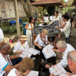 Group of people from different ages weaving intricate brown on white fabric panels in an outdoor courtyard workshop