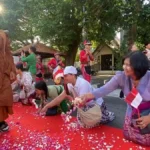 Monks in orange robes walking past a red carpet as people kneel and shower petals indonesian flags in the background
