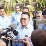 Man in a light blue shirt being interviewed by the press outdoors surrounded by reporters and cameras