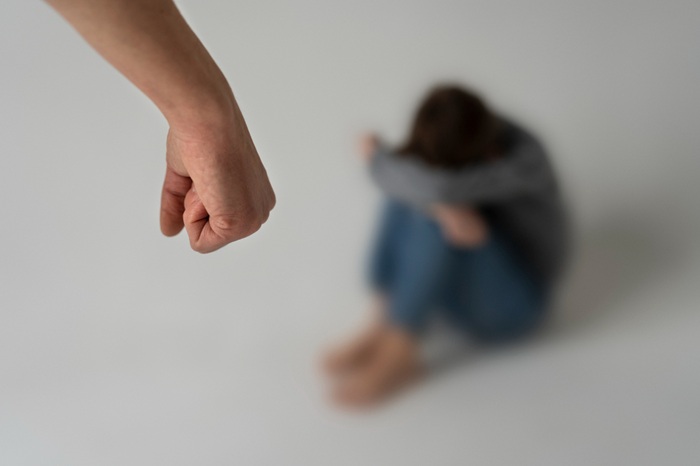 Close-up of a clenched fist reaching toward a person sitting on the floor, conveying a threatening situation.