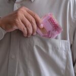 Hand placing pink 100000 banknotes into a shirt pocket