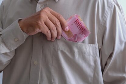 Hand placing pink 100,000 banknotes into a shirt pocket.