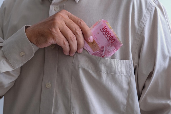 Hand placing pink 100,000 banknotes into a shirt pocket.