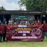 Group of students and instructors pose outdoors holding a maroon banner for a cooperation signing event at a workshop venue in indonesia