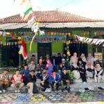Group of people posing on steps outside a green building decorated with colorful banners for a community event indonesian flag in view