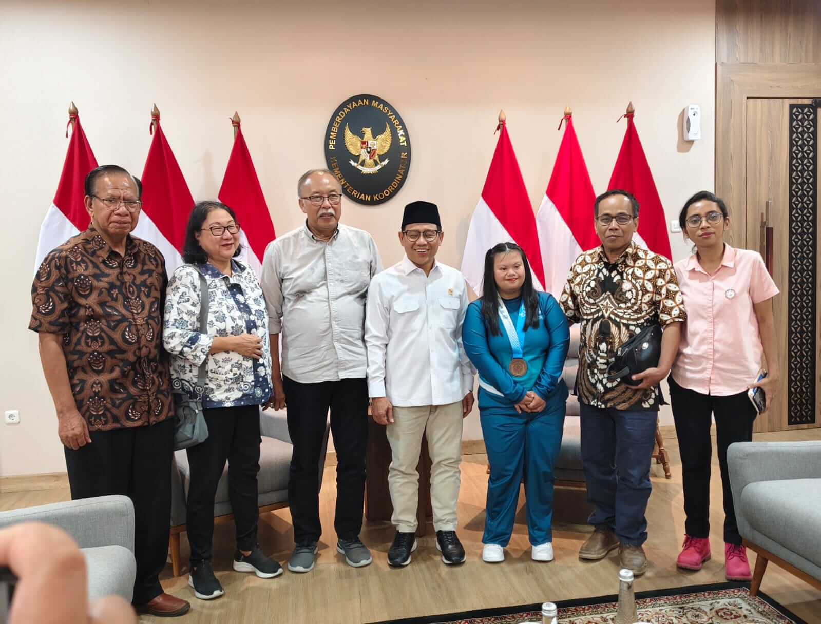 Group of eight people standing in a room with indonesian flags and a government seal behind them posing for a formal photo