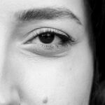 Close up of a womans left eye in blackandwhite showing the eyebrow lashes and a small mole on the cheek