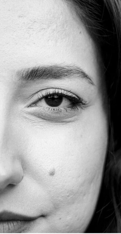 Close-up of a woman's left eye in black‑and‑white, showing the eyebrow, lashes, and a small mole on the cheek.