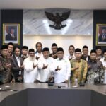 Group of indonesian officials and staff posing in a conference room with the garuda emblem and portraits behind them