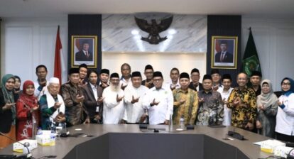Group of Indonesian officials and staff posing in a conference room with the Garuda emblem and portraits behind them.