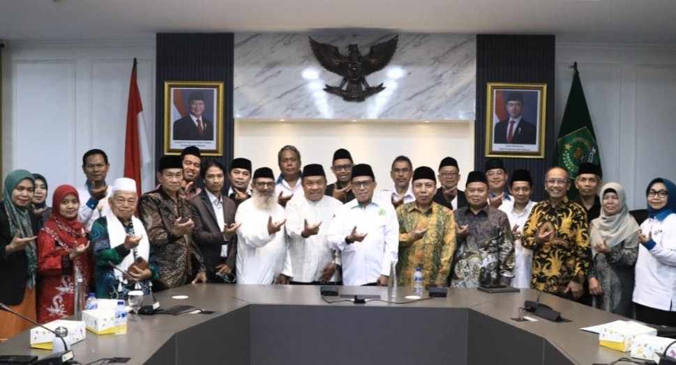 Group of indonesian officials and staff posing in a conference room with the garuda emblem and portraits behind them