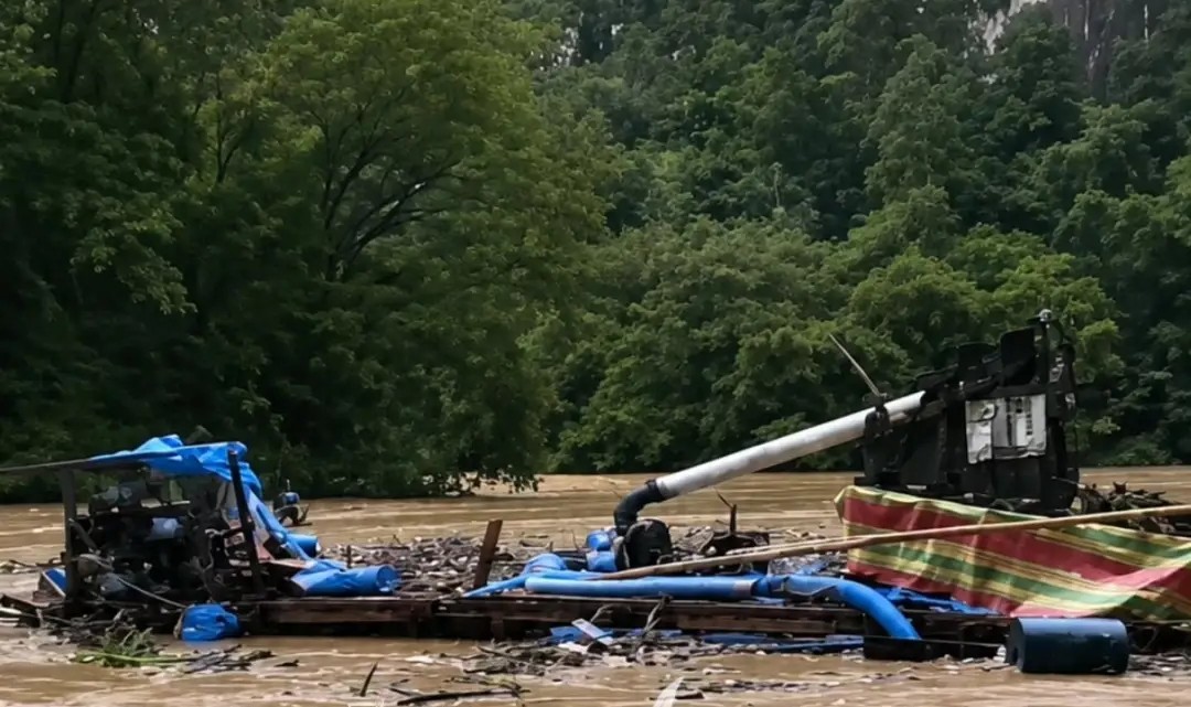 Img20260514wa0003 catrawarta Wrecked boat and scattered debris floating in a muddy floodplain with trees in the background indicating recent flood damage