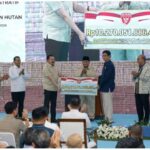 Officials on stage presenting a large ceremonial check to a man wearing a black cap as the audience applauds in front of a banner backdrop with indonesian text rp10 270 051 886 464 shown on the check