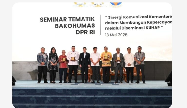 Twelve people on stage at a seminar, each holding a plaque, with a banner behind reading 'SEMINAR TEMATIK BAKOHUMAS DPR RI' and the date '13 Mei 2026'