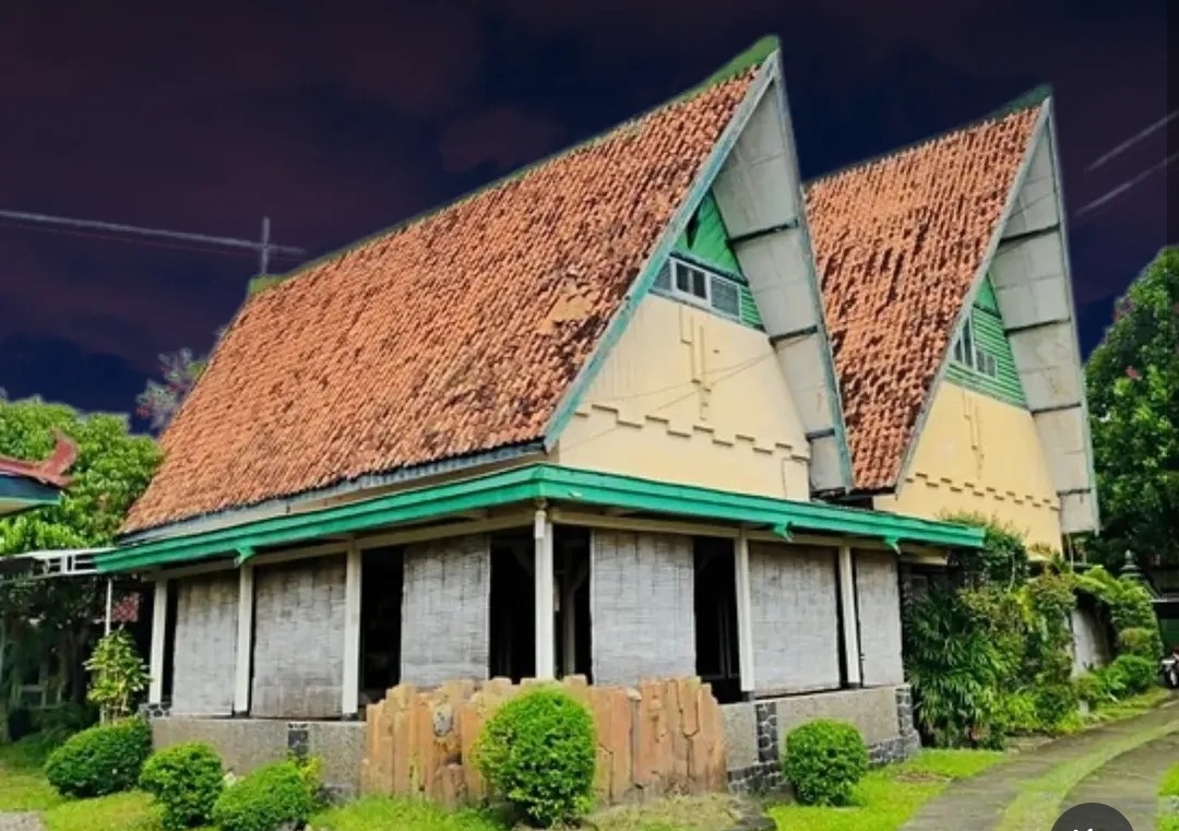 Img20260516wa0007 catrawarta Two a frame buildings with steep orange tiled roofs pale yellow walls and green trim amid a small garden at night
