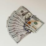 Stack of us $100 bills fanned out on a light surface showing multiple notes spread in a semicircle