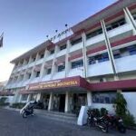 Front view of a white multi story indonesian government building with red accents a flagpole displaying the indonesian flag and motorcycles parked outside