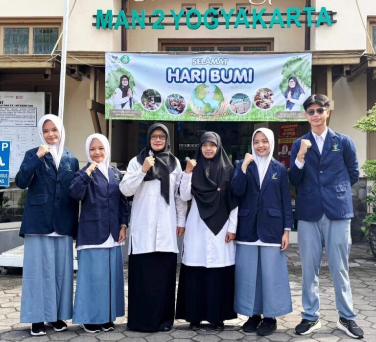 Six students in school uniforms pose with fists raised in front of a banner reading 'Selamat Hari Bumi' outside a building labeled 'MAN 2 YOGYAKARTA'