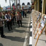 Group of uniformed officers and civilians viewing a row of framed photographs on easels outside a building in a public area