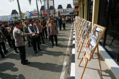Group of uniformed officers and civilians viewing a row of framed photographs on easels outside a building in a public area.