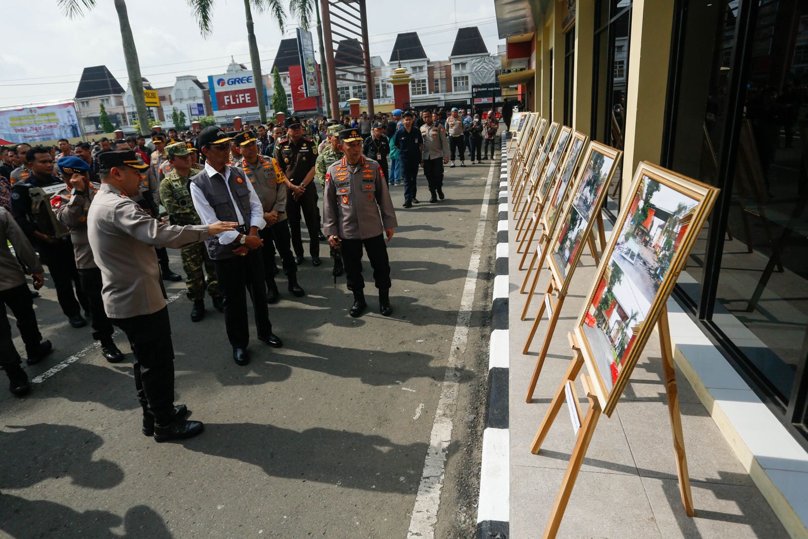 Group of uniformed officers and civilians viewing a row of framed photographs on easels outside a building in a public area