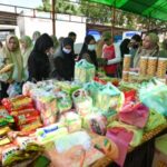 Group of women and people in hijabs at a busy market style stall with stacked food packages and bags of supplies on a table likely a donation drive