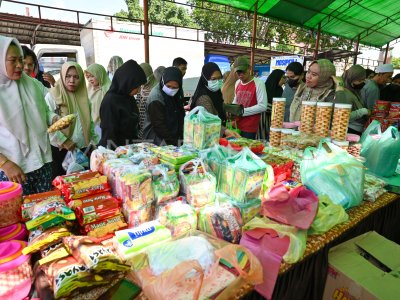 Group of women and people in hijabs at a busy market-style stall with stacked food packages and bags of supplies on a table, likely a donation drive.