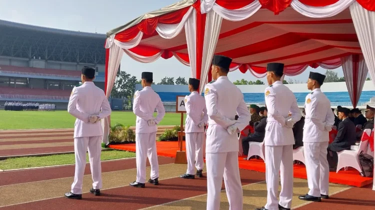 Uniformed men in white dress uniforms stand with hands behind their backs under a red-and-white ceremonial canopy at a stadium ceremony.
