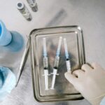Gloved hand handling syringes on a metal lab tray with other medical supplies nearby in a sterile environment