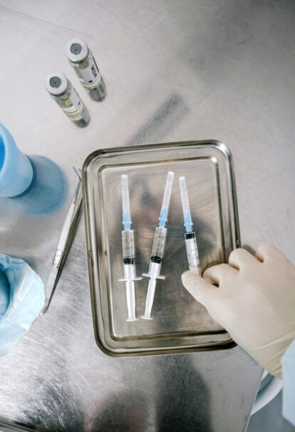 Gloved hand handling syringes on a metal lab tray with other medical supplies nearby in a sterile environment.