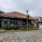 A village scene with two traditional tiled roof houses a cobblestone courtyard and people near the entrance areas