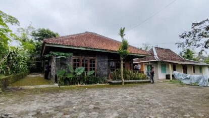 A village scene with two traditional tiled roof houses a cobblestone courtyard and people near the entrance areas