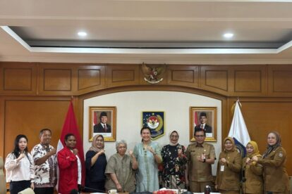 A group of men and women in formal and official attire pose with fists raised in a government meeting room with national symbols on the wall behind them
